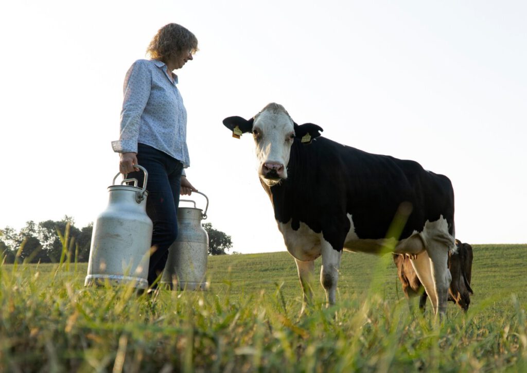 Frau mit Milchkannen und Kuh auf Weide